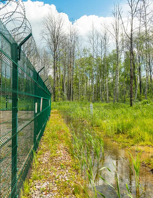 Green anti-climb mesh fence topped with razor wire beside open land